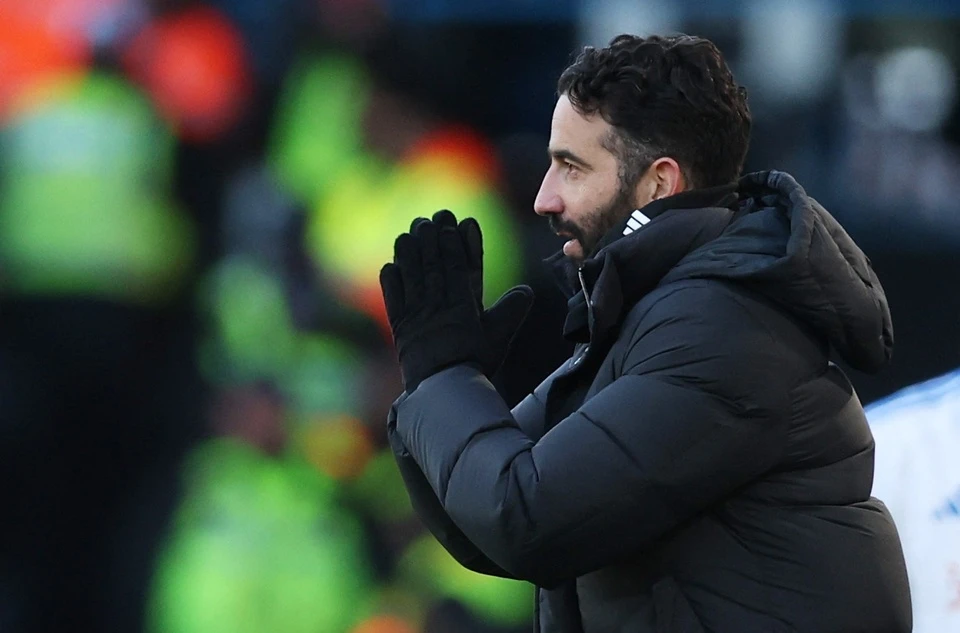 HLV bóng đá mặc áo khoác phao đen chỉ đạo trên sân.